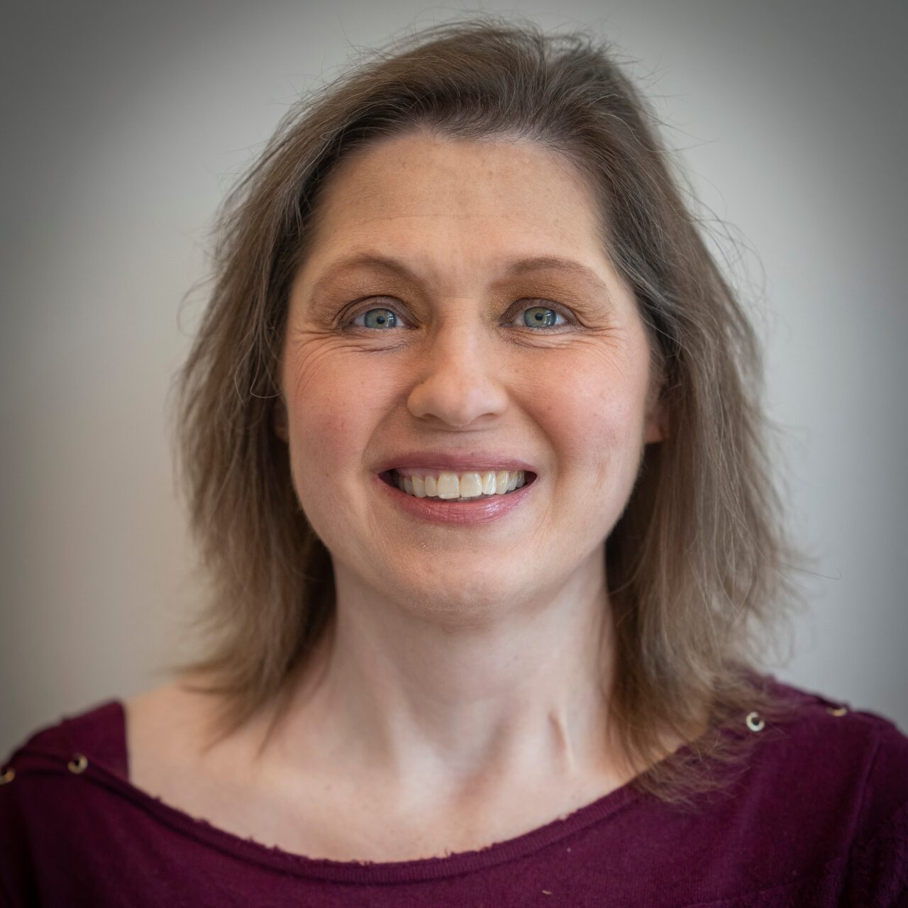 Smiling woman with shoulder-length hair wearing a maroon top.