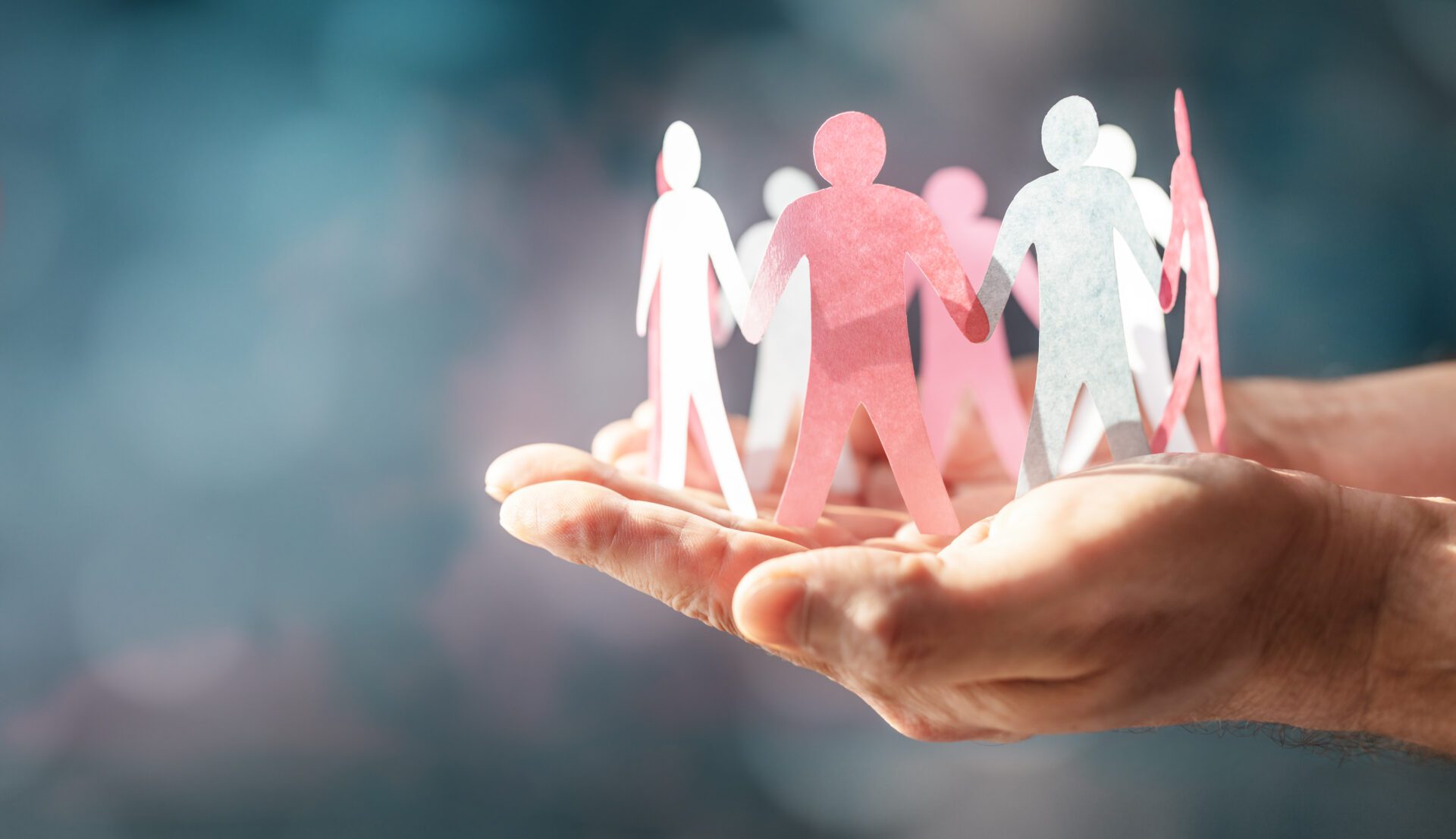 Hands holding paper cutout people figures.