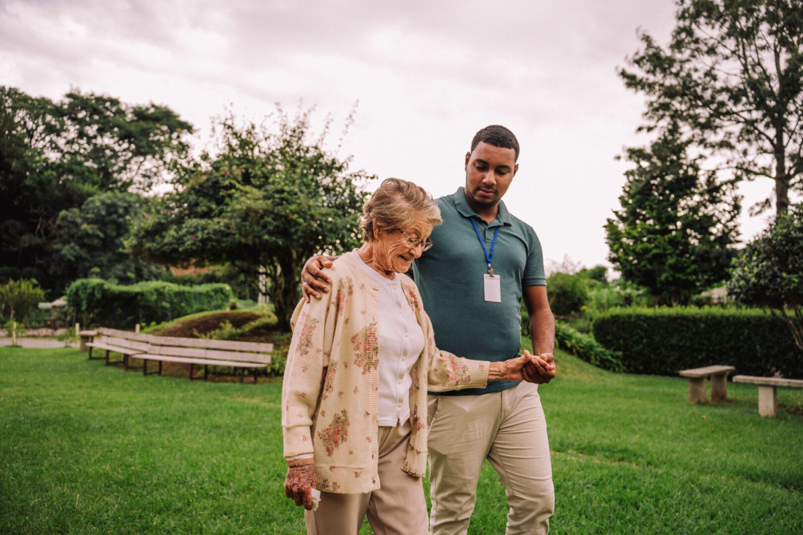 Caregiver assisting elderly woman in garden.